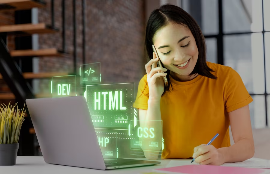 A woman speaking on the phone in front of a laptop screen with graphics related to programming languages