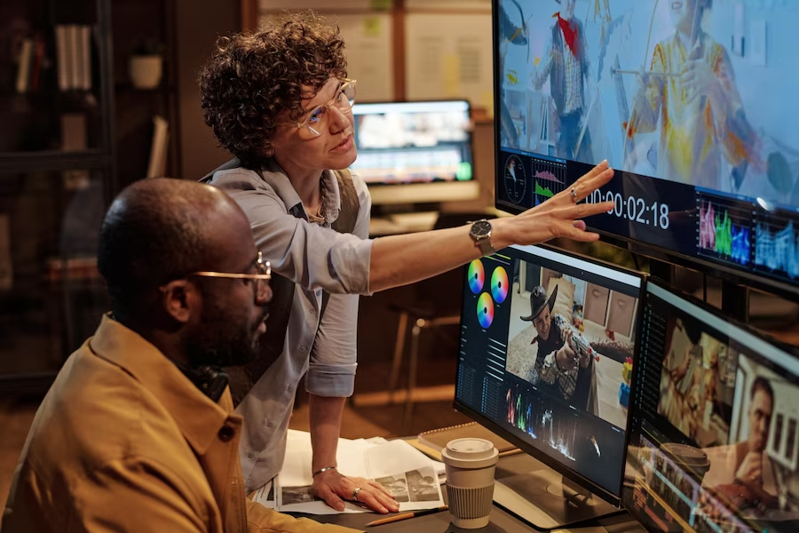 A man and woman in front of multiple editing monitors