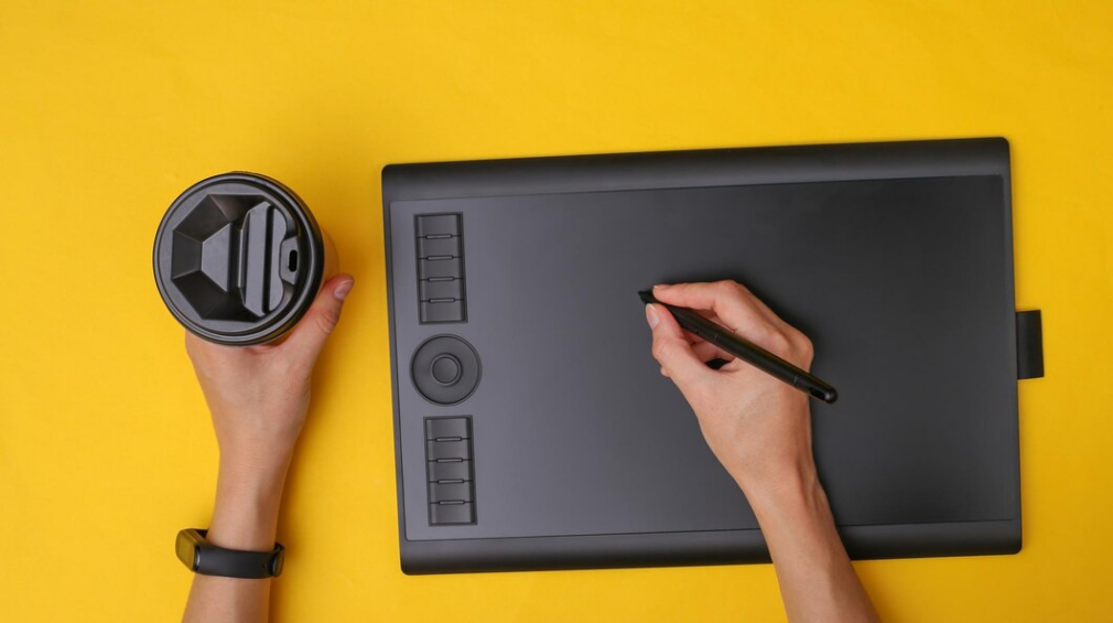 Person with one hand holding a cup and the other hand using a graphics tablet