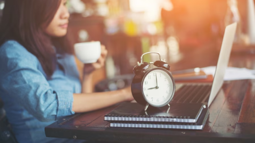 Woman sipping from a mug on a table with an alarm clock nearby