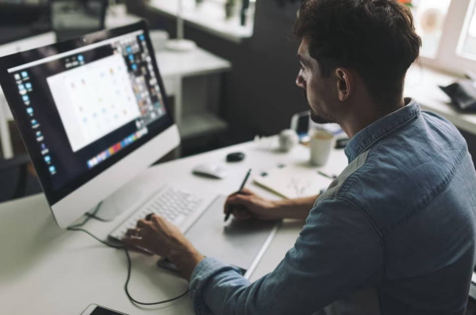 man in a jeans shirt typing on the keyboard and watching on the screen